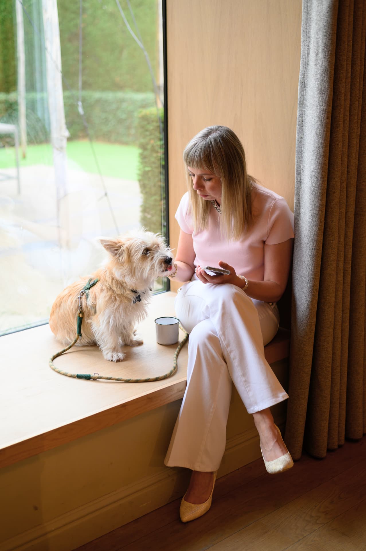 Ethel zit op een brede vensterbank met haar telefoon, haar hond kijkt haar aandachtig aan